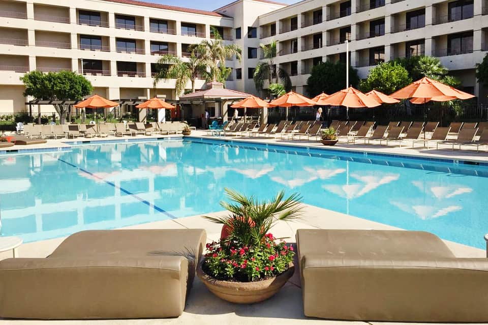 Resort pool with blue water, orange umbrellas, lounge chairs, and multi-story hotel buildings
