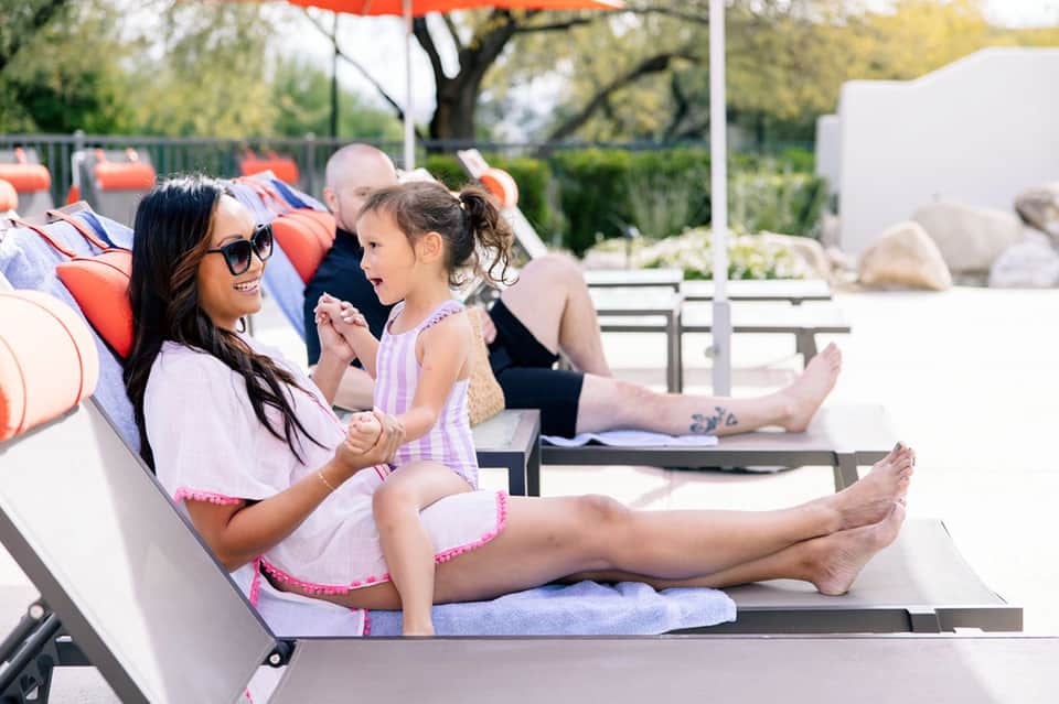 Family relaxing on poolside loungers with colorful umbrellas and landscaped grounds