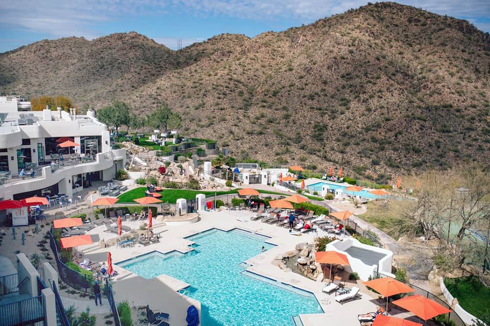 Resort pool area with orange umbrellas nestled against desert mountains and hillside landscape