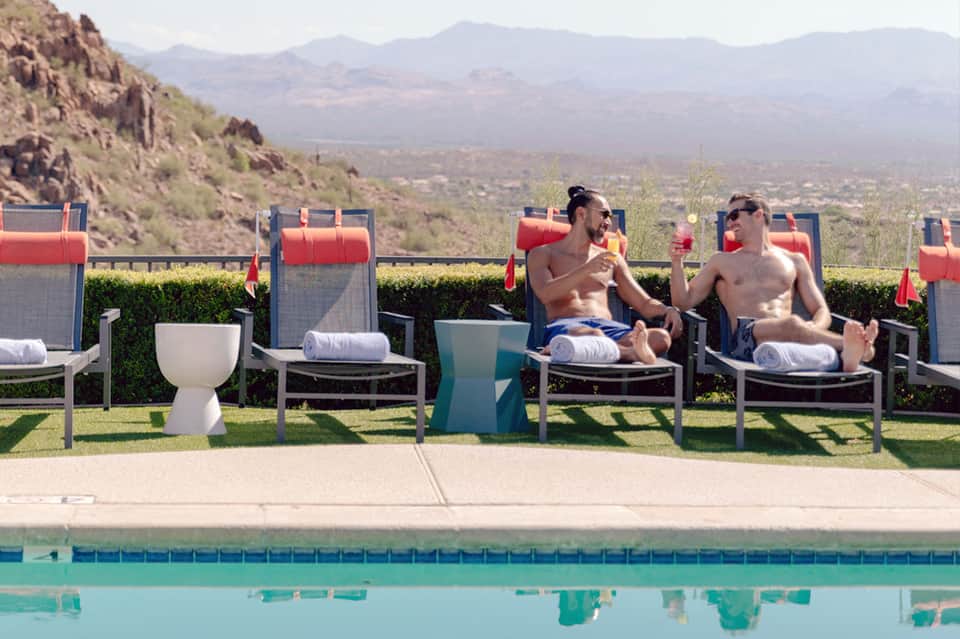 Desert resort pool area with red lounge chairs, sculptural side tables, and mountain valley views