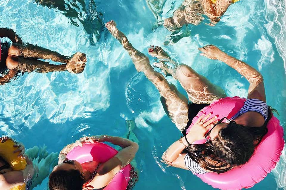 Overhead view of swimmers floating on pink inflatables in crystal clear turquoise water