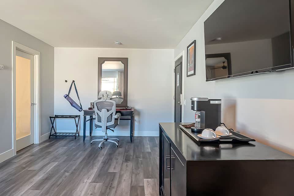 Compact hotel suite showing kitchenette, work desk, chair, and mirror