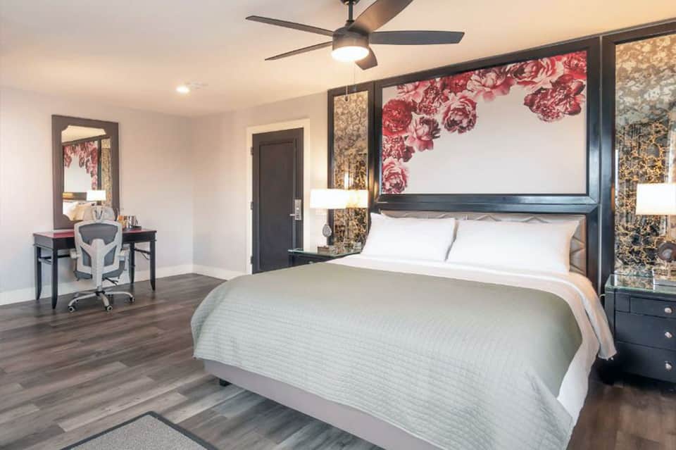 Modern hotel bedroom with queen bed, floral headboard art, and dark wood furnishings