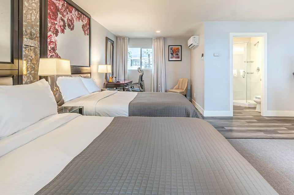 Spacious hotel room with two queen beds, modern furnishings, and ensuite bathroom with ocean view