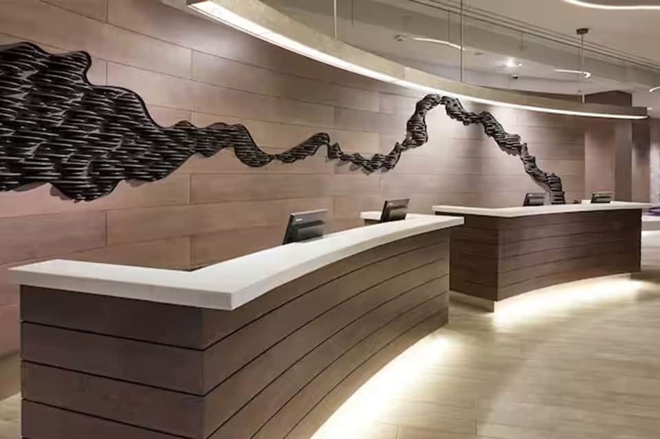 Modern hotel reception desk with curved white countertop and abstract black wave wall sculpture