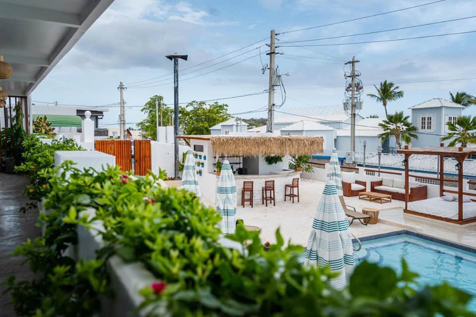 Beachfront resort pool area with striped umbrellas, lounge chairs, and thatched roof structures