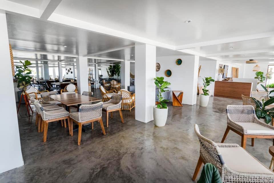 Contemporary hotel lobby with woven chairs, wooden tables, white columns, and plants