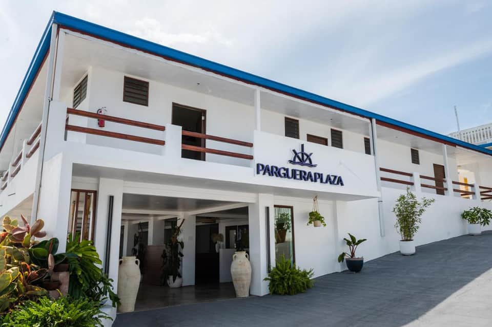 White beachfront hotel building with blue roof and red accents, palm trees entrance