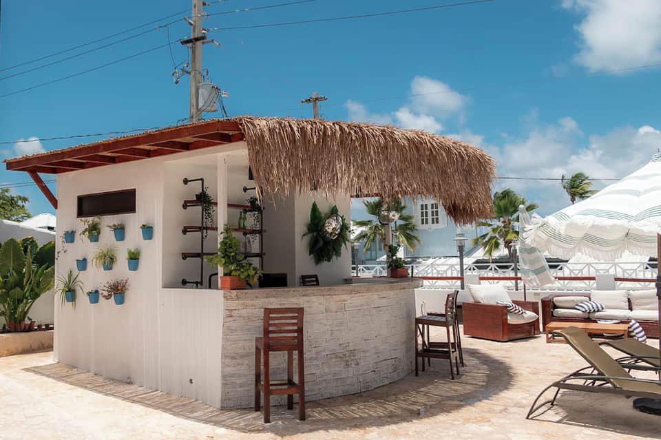 Tiki bar with thatch roof, white walls, potted plants, and beach lounge area with umbrellas