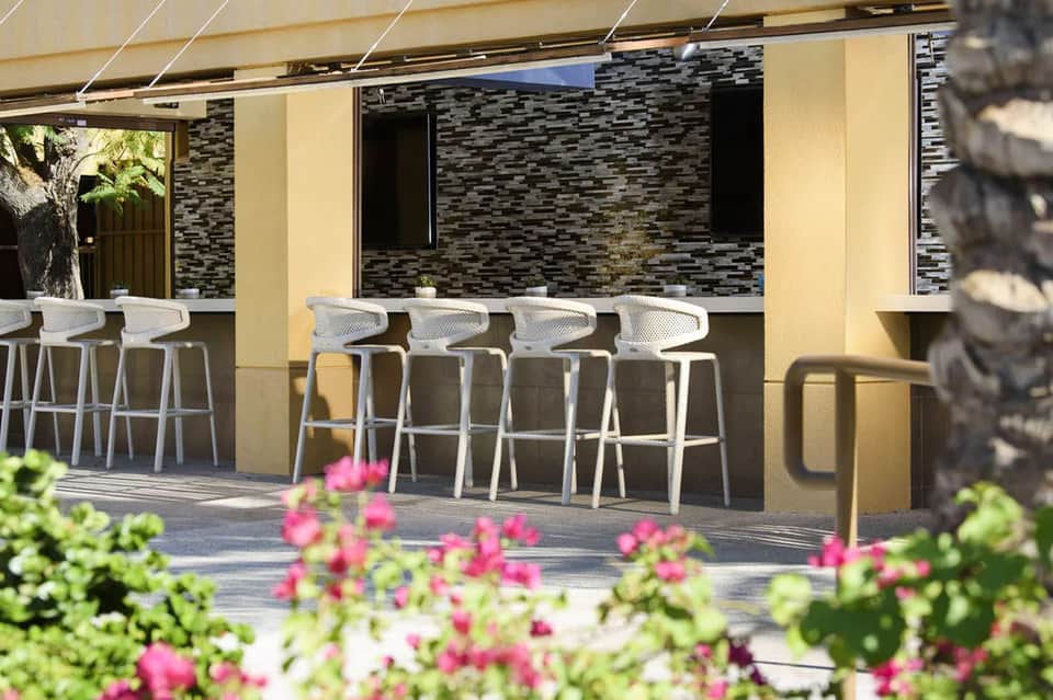 Outdoor bar with white modern stools, stucco walls, and pink flowering plants