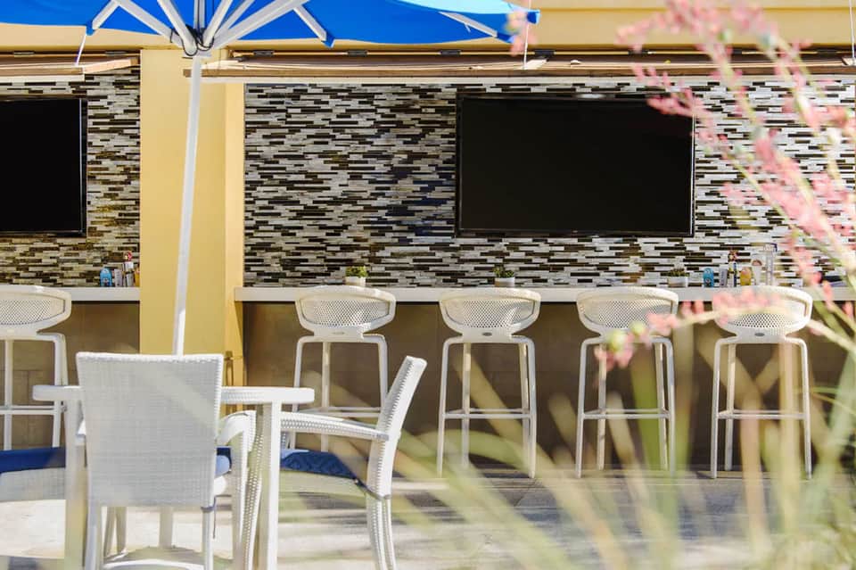 Outdoor bar with white seating, striped blue and white umbrella, and brick backdrop