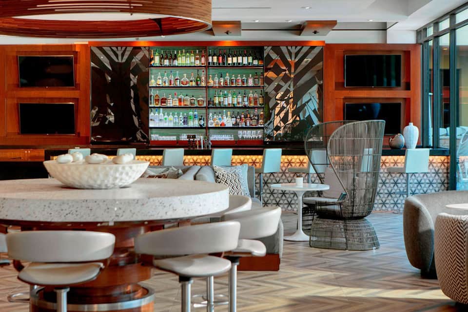 Contemporary bar lounge with red wood paneling, illuminated shelving, and geometric patterned seating