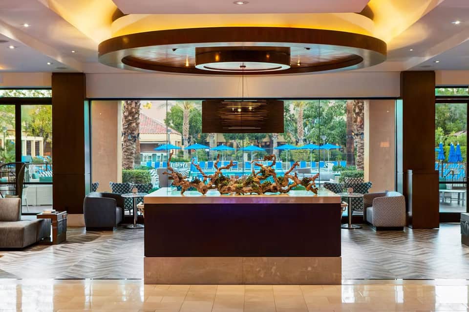 Modern hotel lobby with circular ceiling design, dark wood accents, decorative sculpture, and pool view