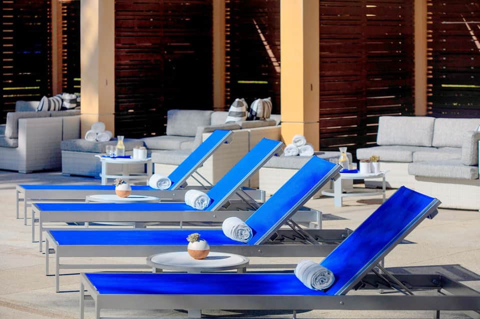 Modern resort deck with blue lounge chairs, gray seating, and dark wooden privacy screens