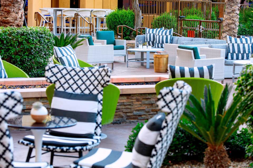 Upscale resort patio with wicker furniture, striped cushions, palm trees, and manicured landscaping