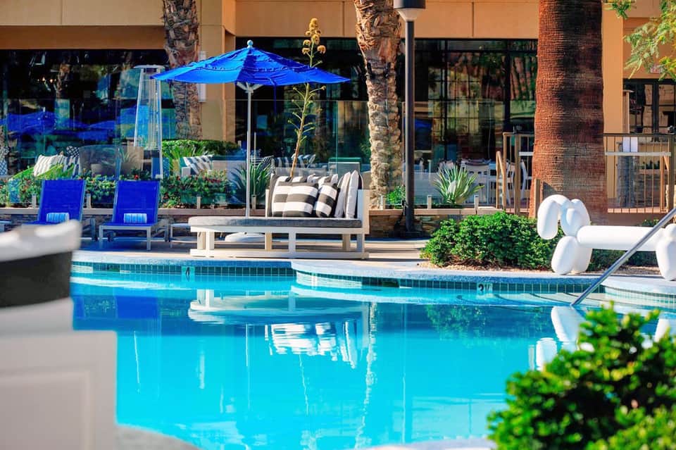 Luxurious poolside patio with blue umbrella, lounge chairs, and palm trees