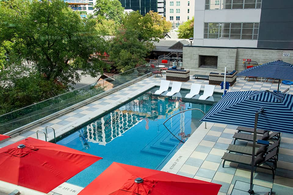 Urban rooftop pool surrounded by colorful umbrellas and lounge chairs