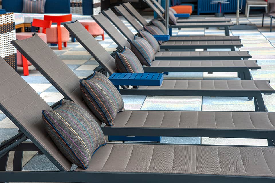 Resort pool deck with gray lounge chairs with striped cushions and colorful accent furniture