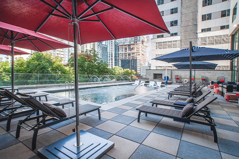 Urban rooftop pool deck with red and blue umbrellas and city skyline views
