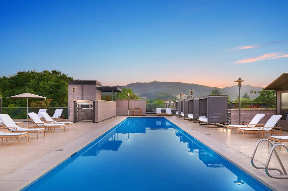 Resort infinity pool at sunset with lounge chairs, modern architecture, and mountain vista