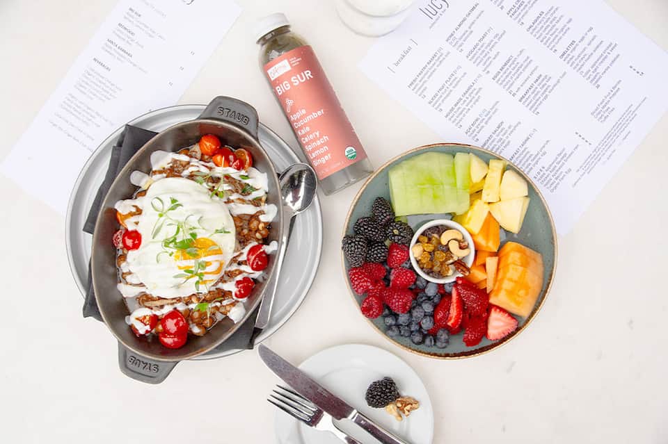 Healthy meal spread with fruit bowl, grain bowl, and organic beverages on white table
