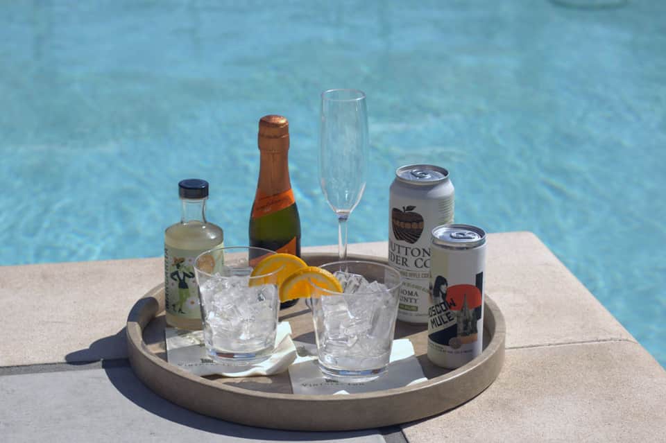 Poolside refreshment tray with bottles, champagne, glasses, and citrus garnishes on concrete deck