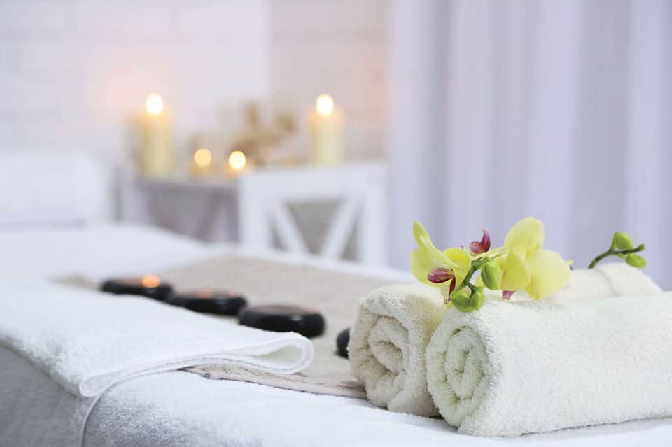 Spa treatment setup with rolled white towels, yellow orchid flowers, black stones, and lit candles