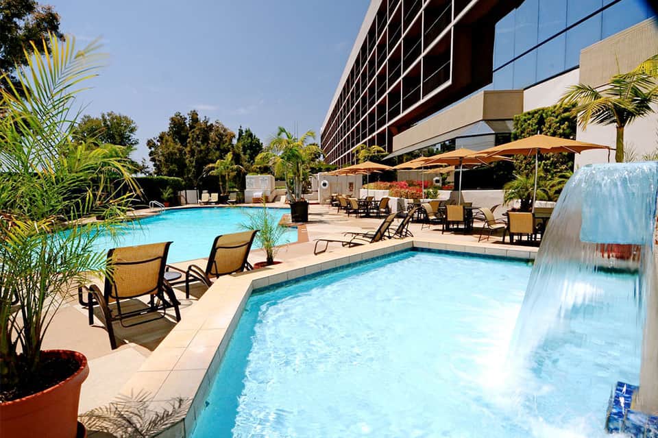Resort pool and spa with lounge chairs, umbrellas, and modern hotel building