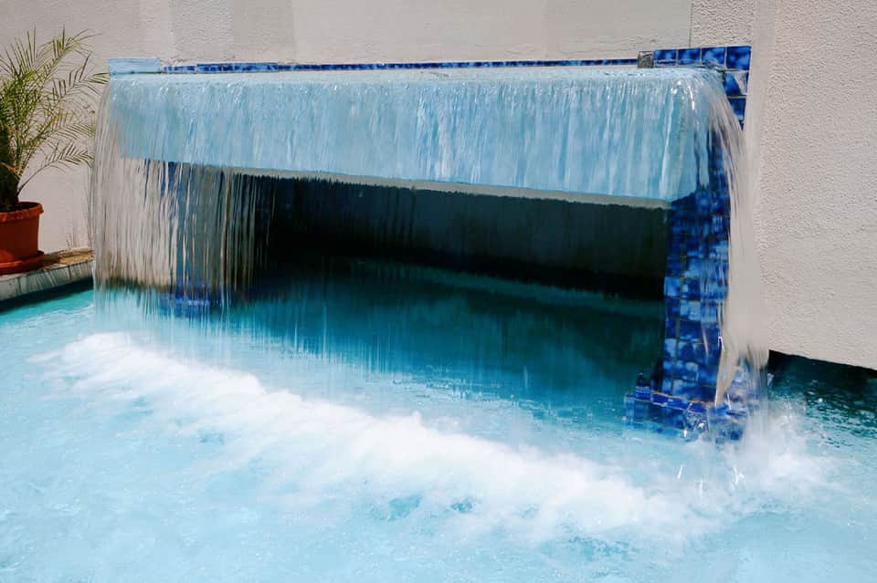 Hot spring or thermal pool with waterfall feature and blue tile surround creating white splash