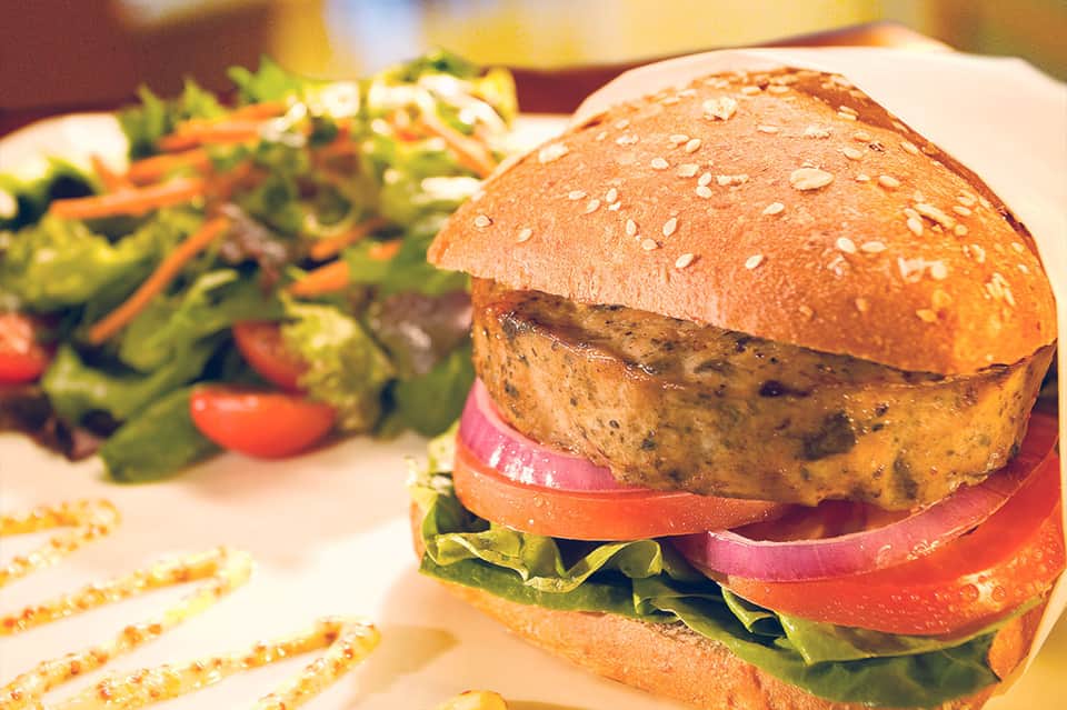 Gourmet burger with sesame seed bun, fresh lettuce and tomato slices on white plate