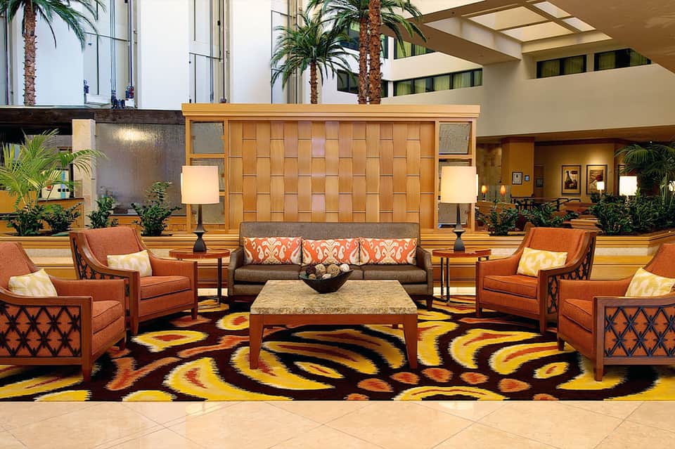 Hotel lobby interior with orange armchairs, colorful patterned rug, and decorative wood wall