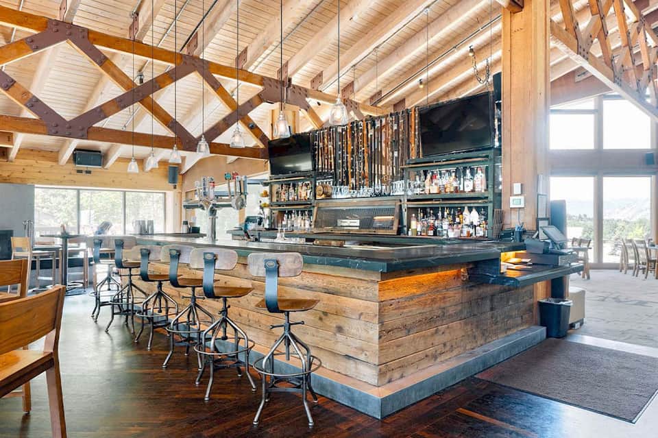 Modern bar with exposed wood beams, dark bar counter, and large windows overlooking landscape