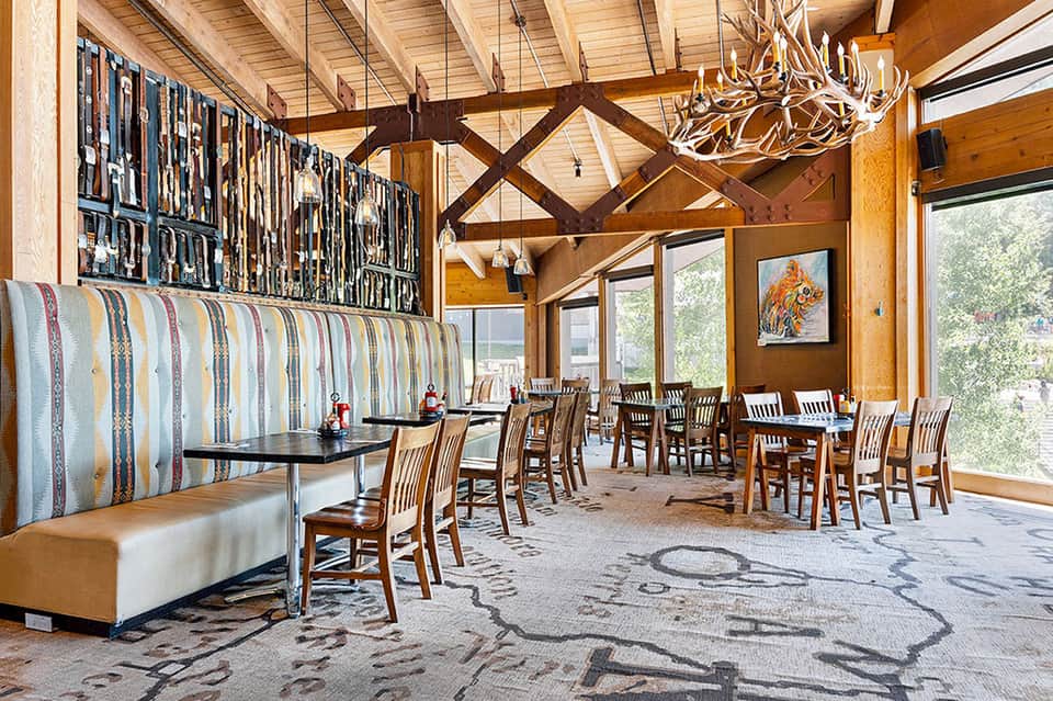Rustic dining hall with exposed wooden beams, fireplace, and large windows overlooking nature