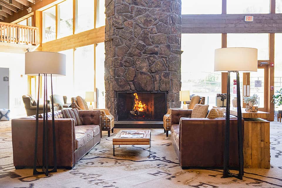Grand hotel lobby with stone fireplace, wooden beams, brown leather seating, and floor lamps