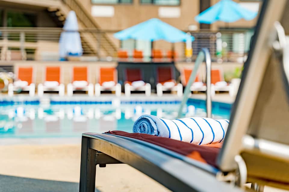 Close-up of rolled towel on lounge chair overlooking resort pool with orange chairs and umbrellas