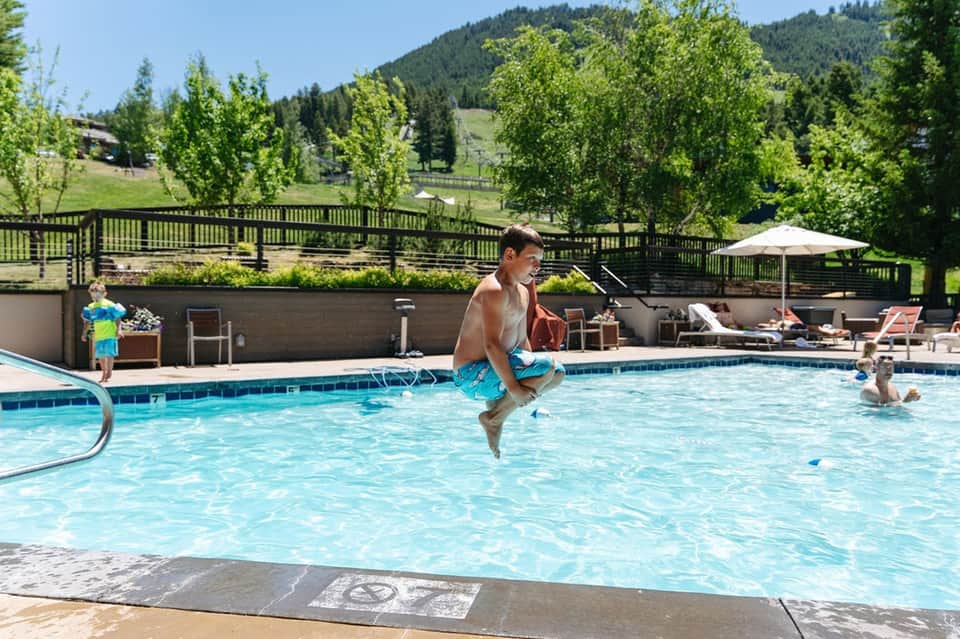 Boy cannonballing into mountain resort pool with forest backdrop