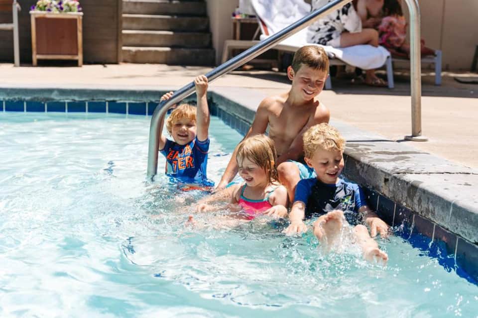 Children playing and swimming in a resort pool with happy supervision nearby