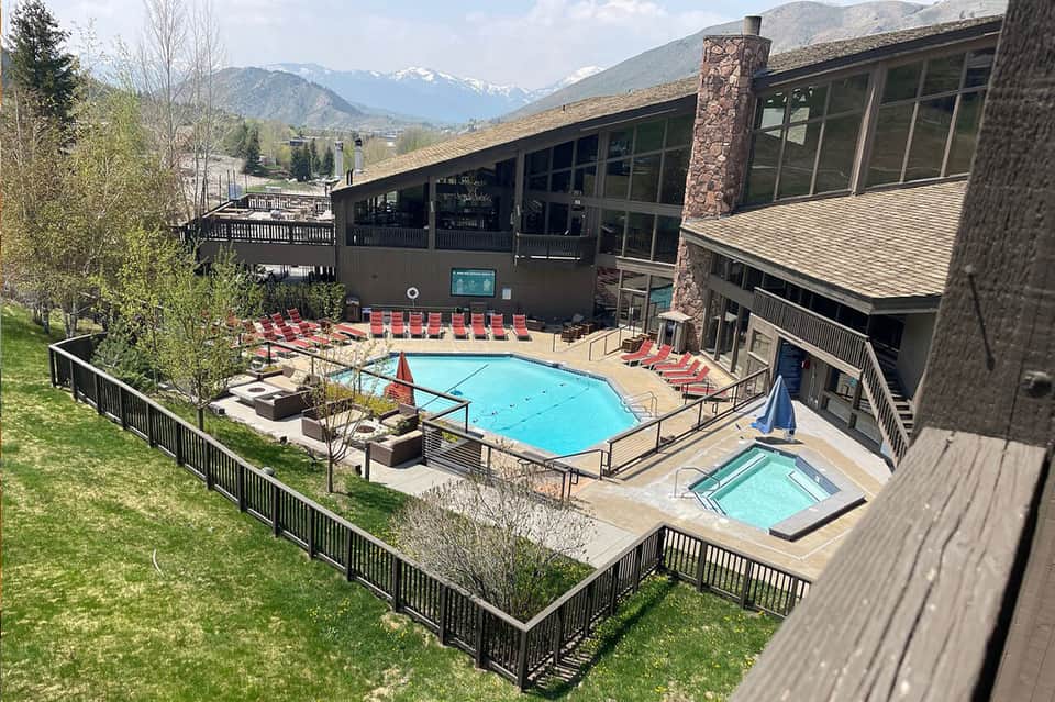 Mountain resort pool with red lounge chairs, snow-capped peaks visible in background
