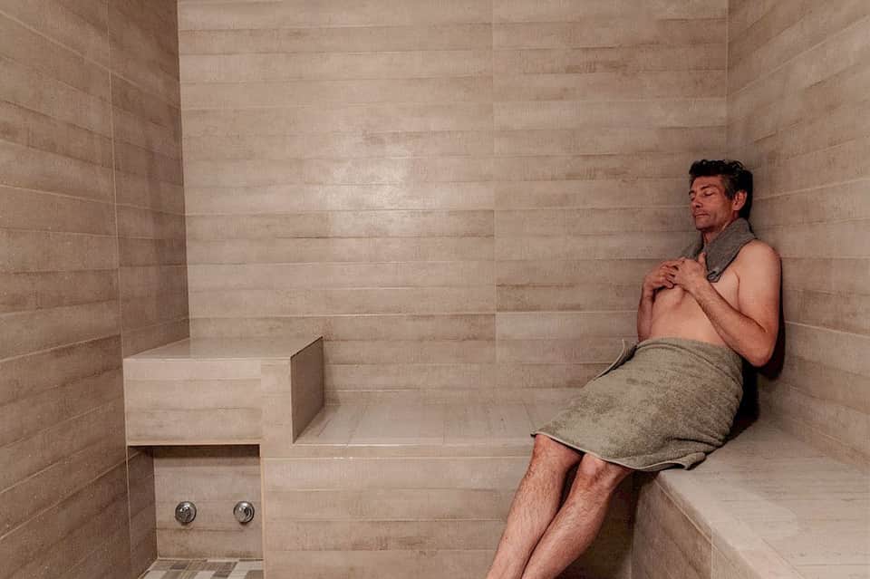 Man relaxing in a modern sauna with tile walls and built-in wooden bench seating