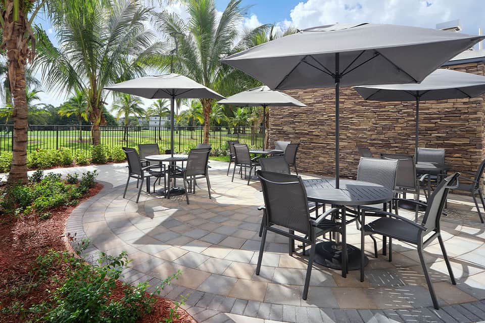Outdoor patio with black lounge chairs, gray umbrellas, palm trees, and stone accent wall