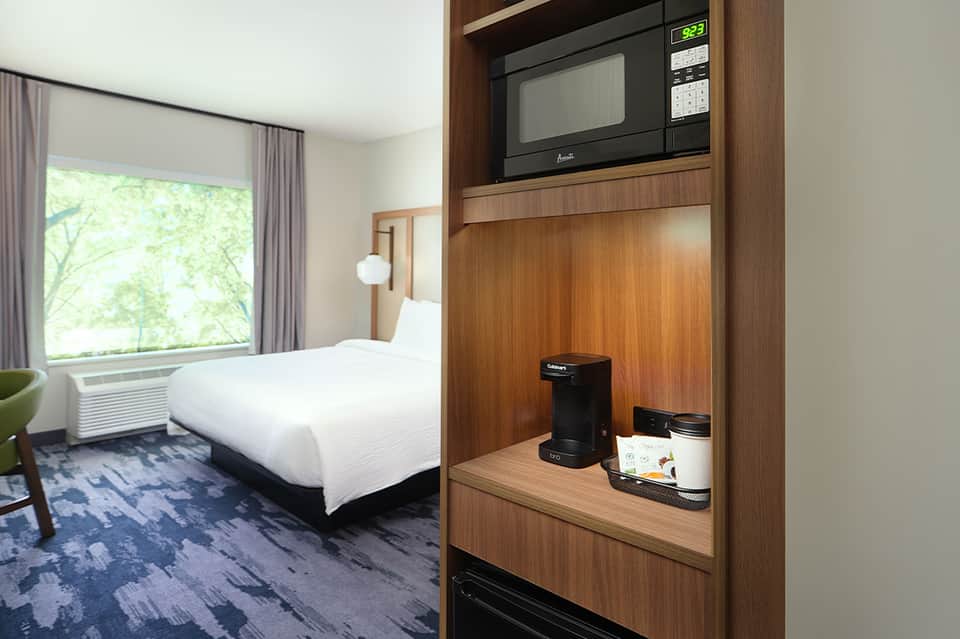 Modern hotel room with bed, wood cabinetry, and microwave setup