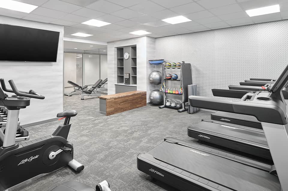 Modern gym interior with cardio equipment, free weights, mirrored studio space, and TV screens