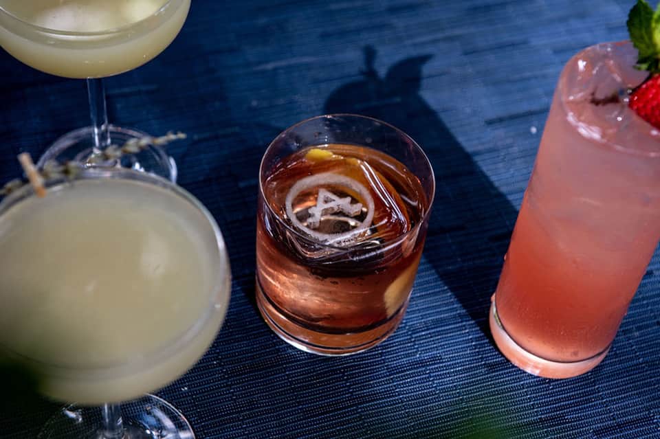 Three colorful cocktails on blue surface with mint garnish and ice