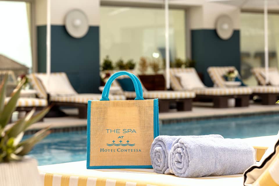 Hotel spa tote bag and white rolled towels poolside with lounge chairs visible behind