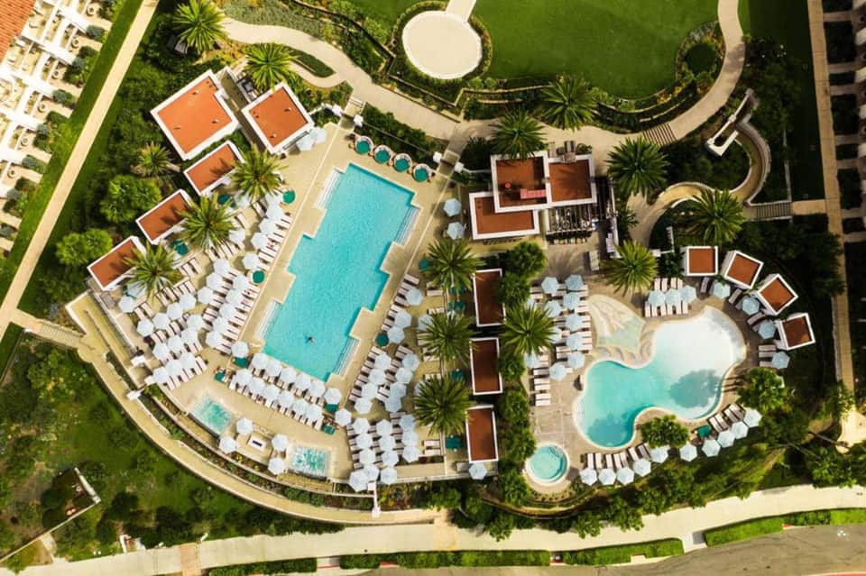 Aerial view of large resort complex with multiple pools, palm trees, and manicured grounds