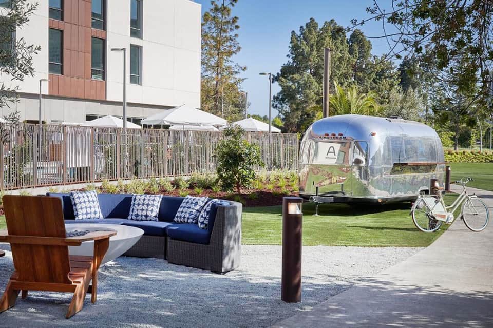 Modern resort patio with blue sectional sofa, vintage Airstream trailer, and manicured lawn