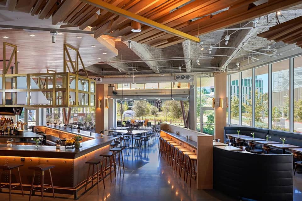Contemporary restaurant interior with exposed wooden beams, multiple bar areas, floor-to-ceiling windows