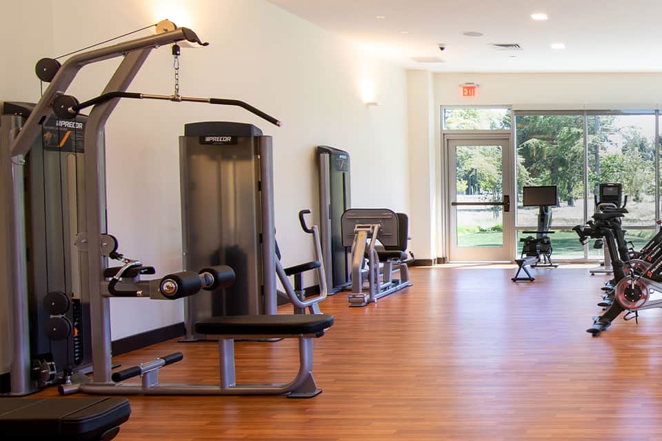 Modern fitness center with cardio equipment, stationary bikes, and large windows overlooking green grounds.