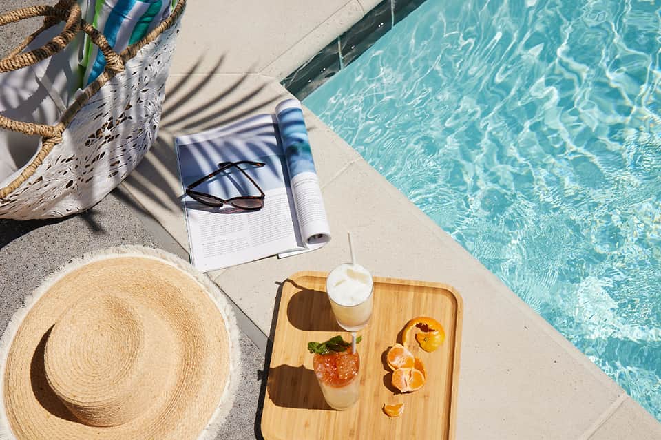 Poolside relaxation setup with straw hat, book, sunglasses, and tropical drink