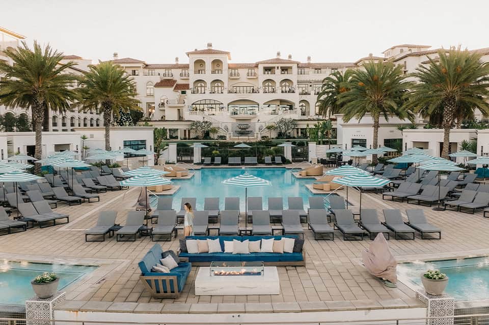 Luxury resort pool with pale blue water, loungers with umbrellas, and Mediterranean architecture